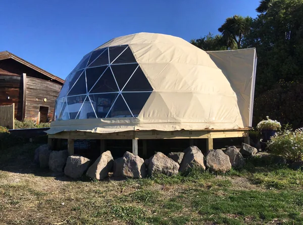 Dome op houten palen naast een houten schuur