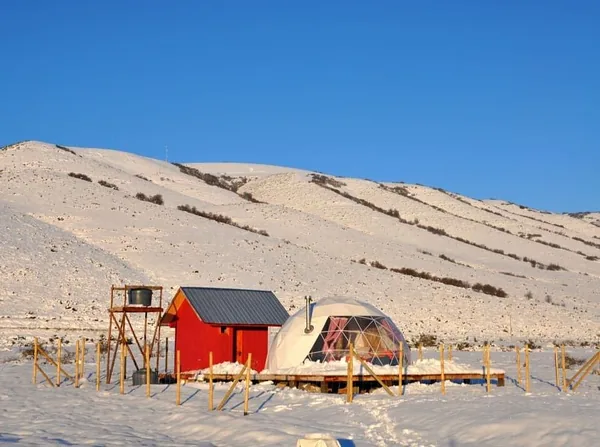 Dome en houten bijgebouw in de sneeuw met besneeuwde heuvels erachter