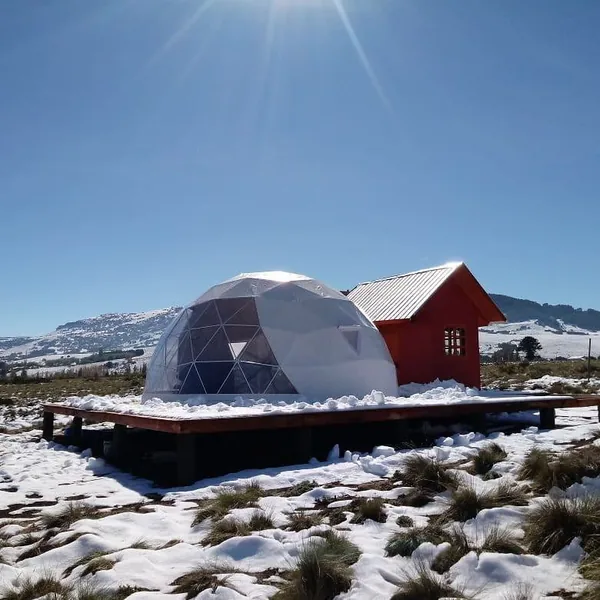 Dome naast een rood huisje in een besneeuwd landschap
