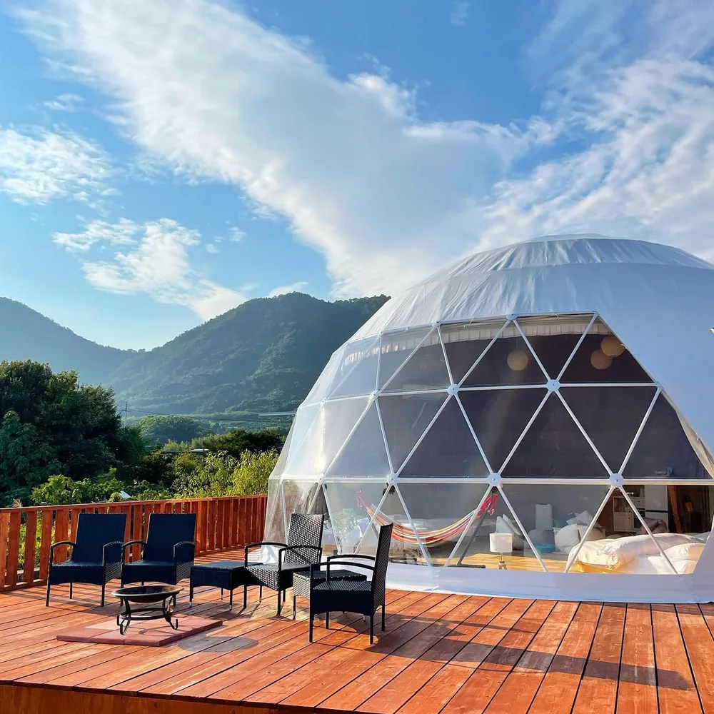 Dome op een ruim houten terras met loungestoelen en bergen op de achtergrond