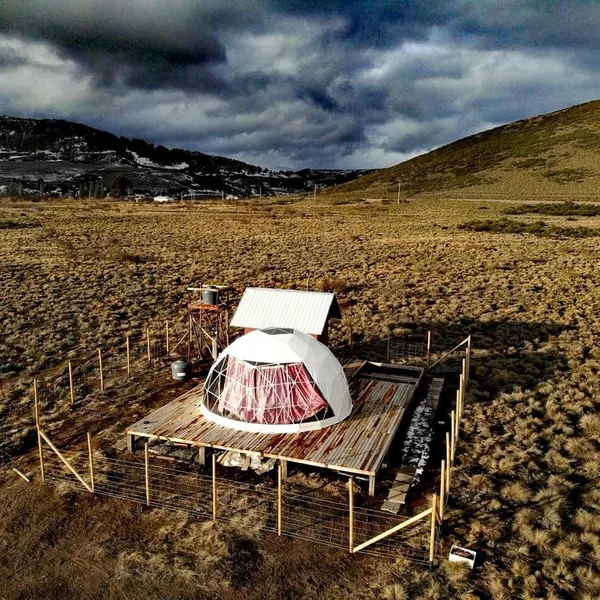Dome op een houten vlonder in een open landschap, van bovenaf gezien