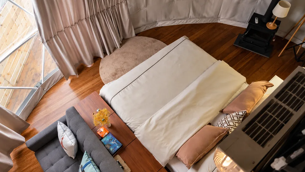 Bovenaanzicht van een domeinterieur met bed, bank en houtkachel