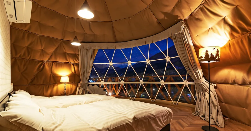 Slaapkamer in een dome bij avond, met sterrenhemel door het panoramaraam