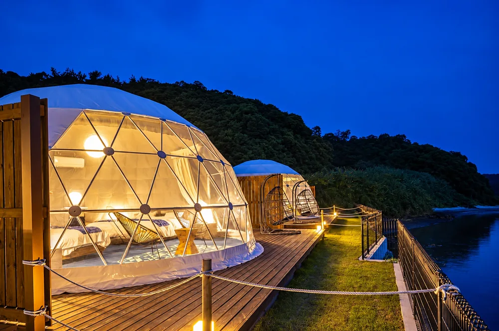 Twee verlichte domes op een houten vlonder aan het water in de schemering
