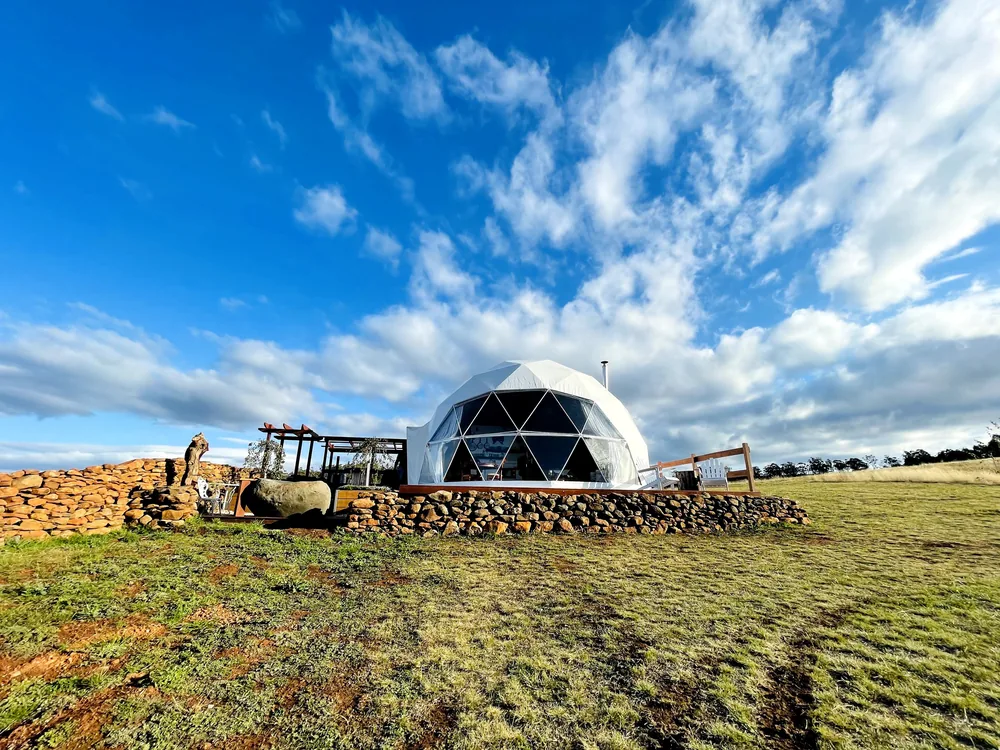 Geodetische dome in een open grasveld onder een strakke wolkenlucht