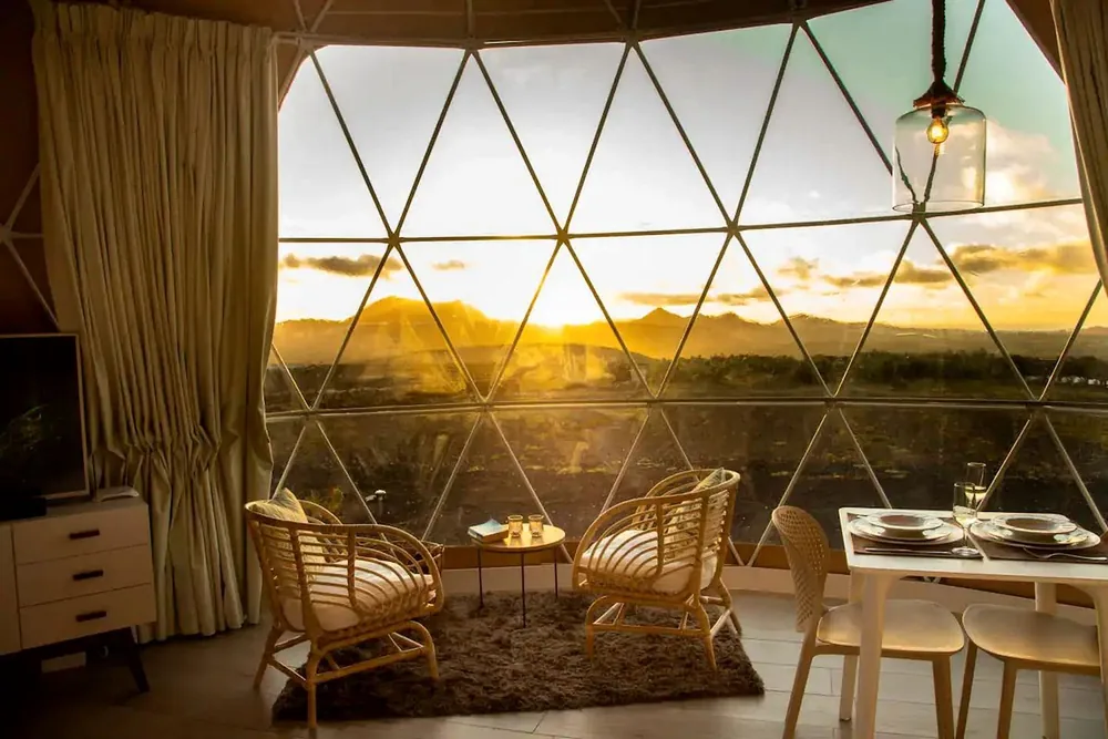 Zithoek in een dome met rieten stoelen en avondzon door het panoramaraam